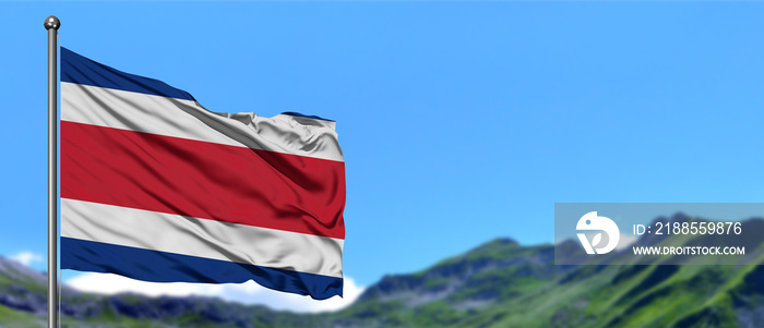 Costa Rica flag waving in the blue sky with green fields at mountain peak background. Nature theme.