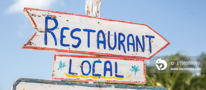 A sign saying Local Restuarant points to the right in a tropical summer destination, written on a rustic wooden white board