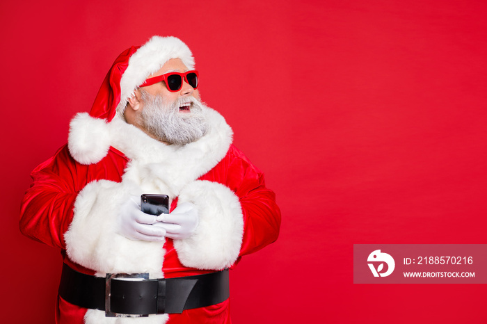 Portrait of cheerful santa claus in hat looking dreamy using cell phone plan newyear party wearing b