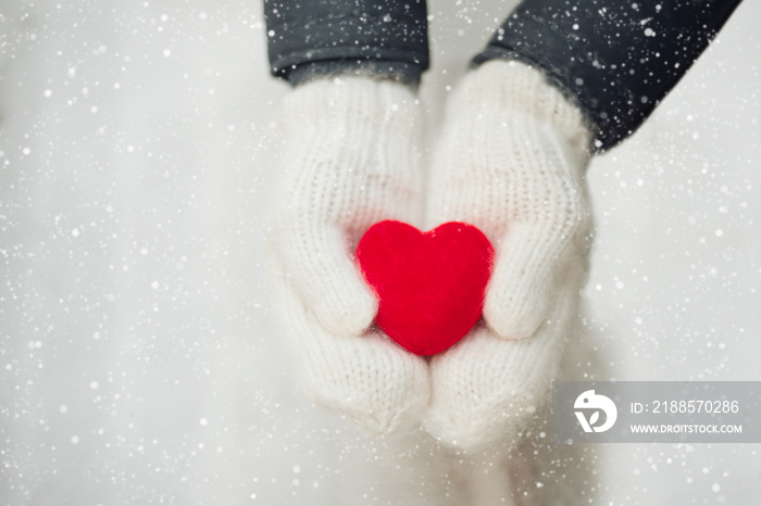 Red heart in womans hands wearing white woolen mittens. Valentines Day concept