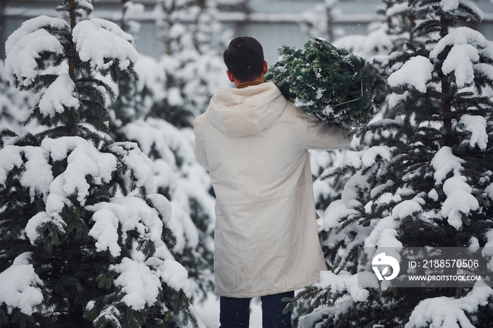 Young handsome man carrying fresh cutted fir tree outdoors