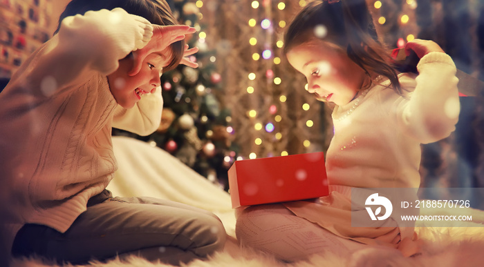 Family on Christmas eve at fireplace. Kids opening Xmas presents. Children under Christmas tree with