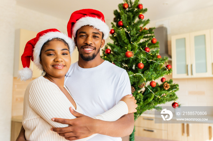 latin hispanic couple hugging each other near the christmas tree at home