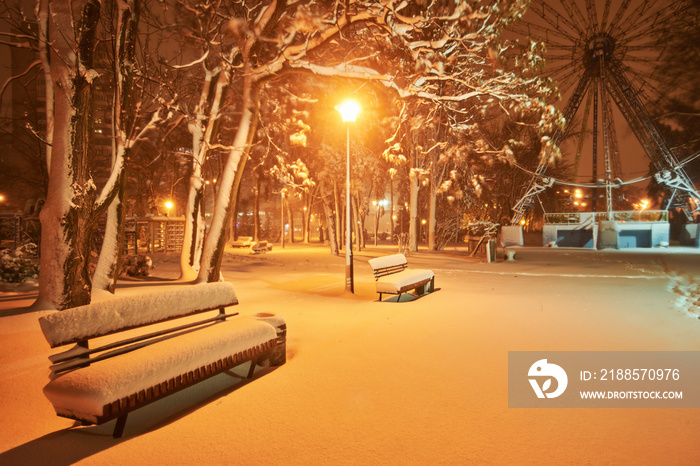 View of bench against christmas tree and shining lantern through snowing.