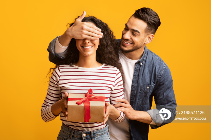 Surprise Gift. Romantic arab man covering his girlfriends eyes and giving present