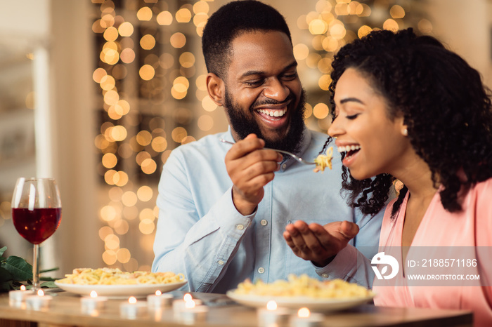 Smiling black man feeding his woman on a date