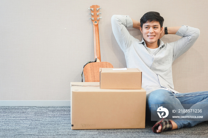 close up young student asian man sitting with box and guitar prepare for decor in new residence , mi