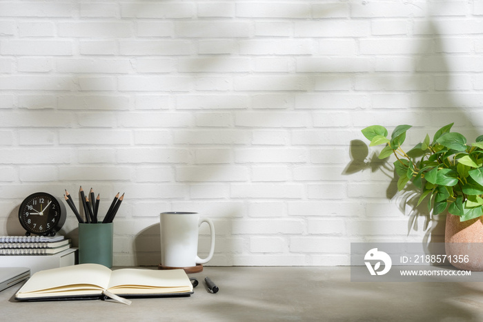 Home office desk with books, cup of coffee, stationery and potted plant on grey table.