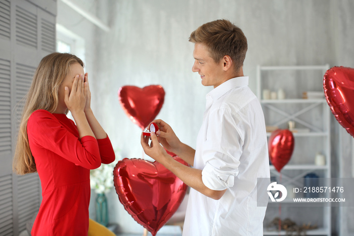 Young man proposing to his beloved with beautiful engagement ring at home