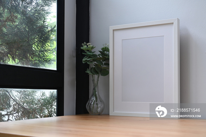 White photo frame and potted plant on wooden table near window.