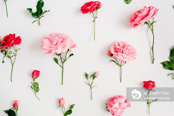 Floral pattern made of pink and red roses, green leaves, branches on white background. Flat lay, top