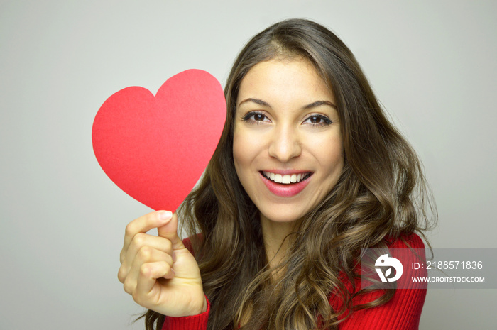 Valentines Day. Beautiful young woman wearing red dress and holding a paper red heart on gray backg