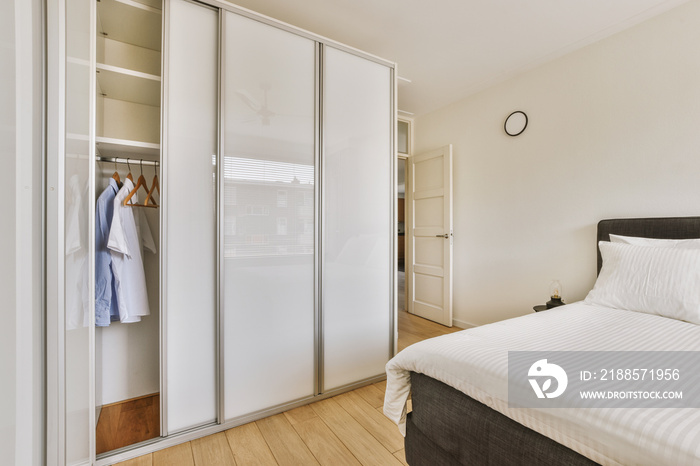 Home interior design of bedroom with bed and wooden wardrobe placed in corner near window in modern 