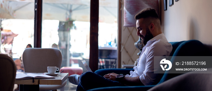 Smiling young man using laptop at a cafe.