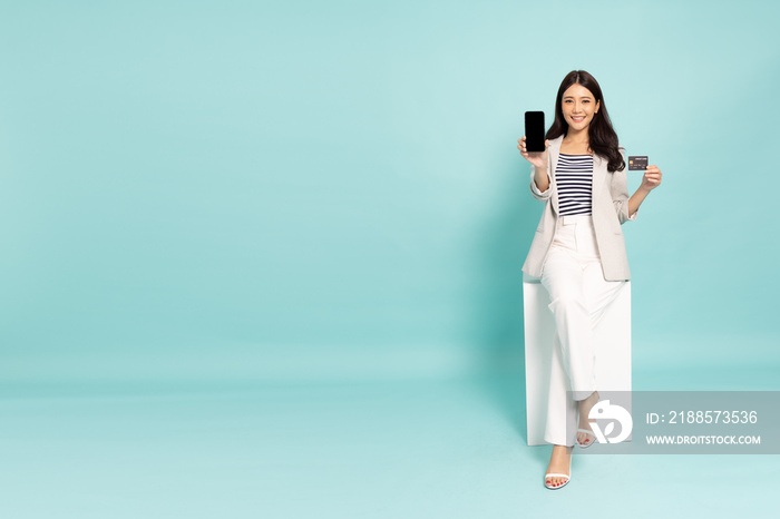 Young Asian businesswoman sitting and showing credit card and mobile phone isolated on green backgro