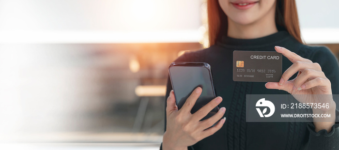 Smiley young woman holding credit card and using smartphone, banner background, online payment.