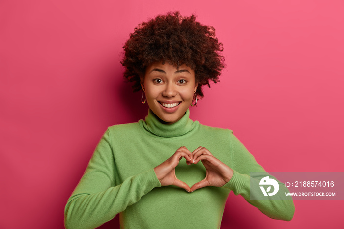 Pleased cheerful dark skinned Afro American woman shapes heart, confesses in love and expresses symp