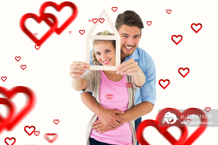 Young couple hugging and holding house outline against hearts