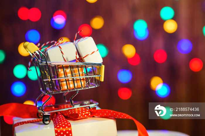 Shopping cart with Christmas box. Valentines gifts. Color bokeh background. Christmas sales. Merry 