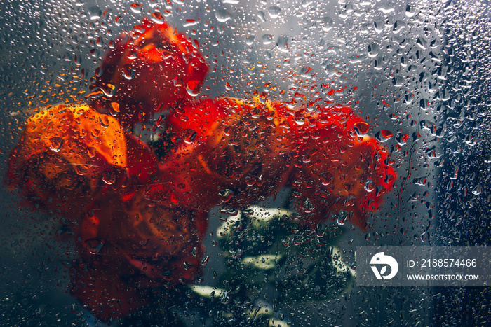 Bunch of beautiful faded flowers through the glass with rain drops