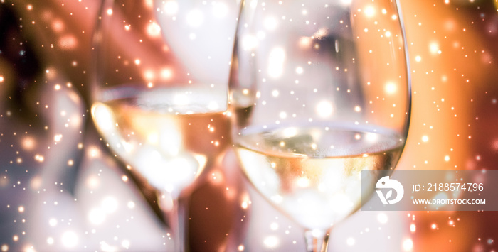 Winter holiday glasses of white wine and glowing snow on background, Christmas time romance