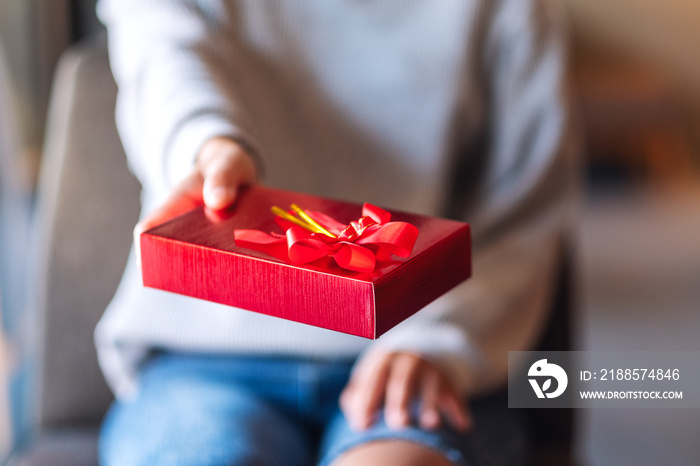 Closeup image of a woman holding and giving a red present box