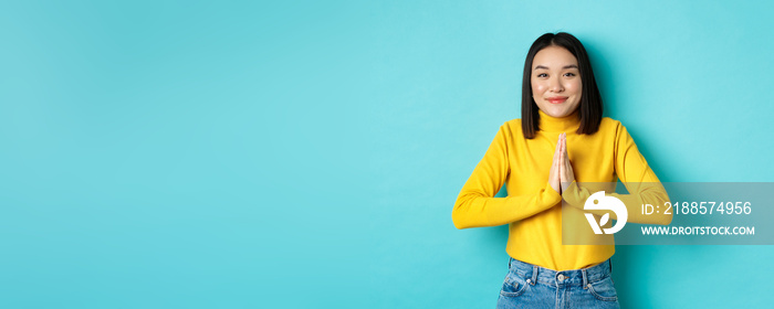 Cute asian woman in trendy outfit saying thank you, holding hands in namaste, begging gesture, smili