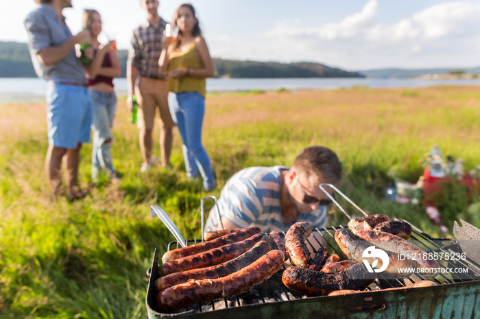 Grillparty mit Würstchen auf einer Wiese am See, Männer und Frauen