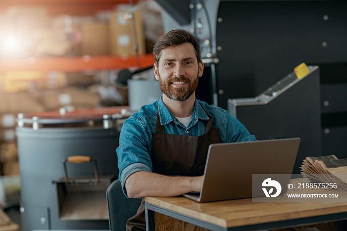 Warehouse worker of small coffee roasting factory working laptop on his workplace