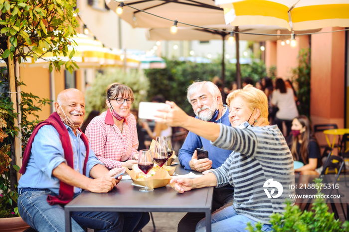 Senior couples drink red wine at bar with face masks protection - New normal lifestyle concept with 