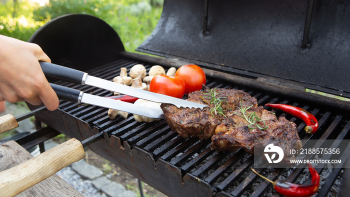 Beef steaks cooking on the charcoal grill with chili pepper, tomatoes, garlic and mushrooms for bbq 