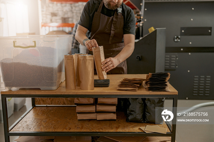 Close up of male barista hands weighs paper bag with coffee beans on a scale at coffee factory