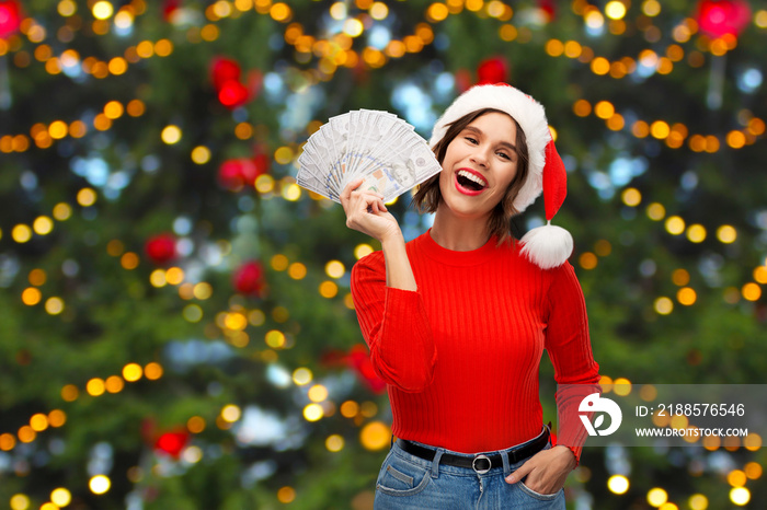 winter holidays and finance concept - happy smiling young woman in santa helper hat holding dollar m