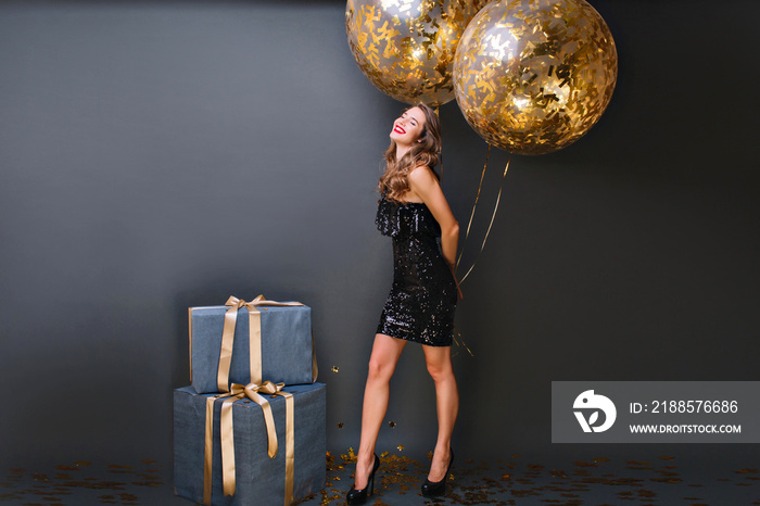 Enthusiastic white girl with sparkle helium balloons enjoying  birthday photoshoot on dark backgroun