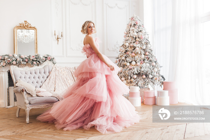 Young beautiful blond woman on christmas background full height. Attractive lady in pink gorgeous dr