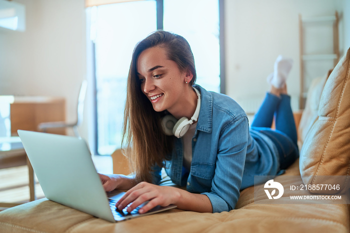 Casual smart modern smiling millennial girl with wireless headphone using laptop for watching video 