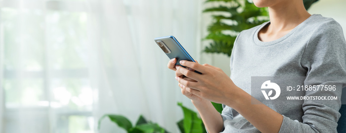 Woman hands using smartphone with typing on social and sitting on sofa in living room.