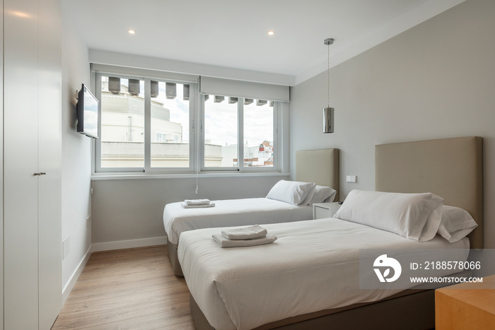 Bedroom with two separate beds with towels and white cabinets, wall tv and large window with a view 