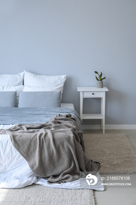 Table with houseplant and big bed near grey wall