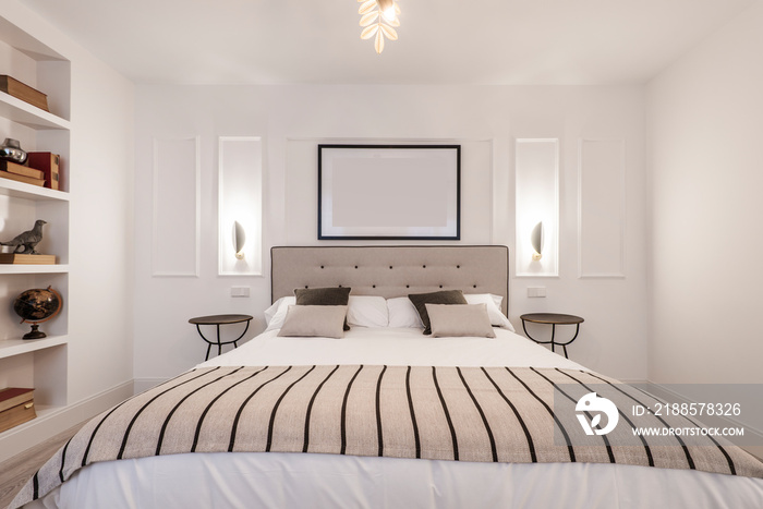 Bedroom with headboard upholstered in beige fabric, matching blanket, twin bedside tables and plaste