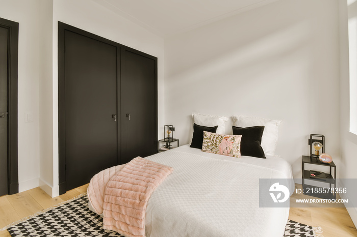 a bedroom with white walls and black closets on the wall behind the bed is a pink throw pillow that