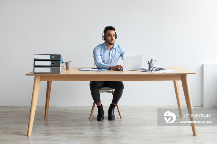 Arab man using laptop wearing headset sitting at desk