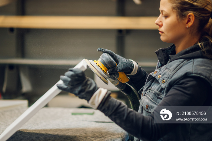 Woman carpenter using an electric sander in a workshop or factory