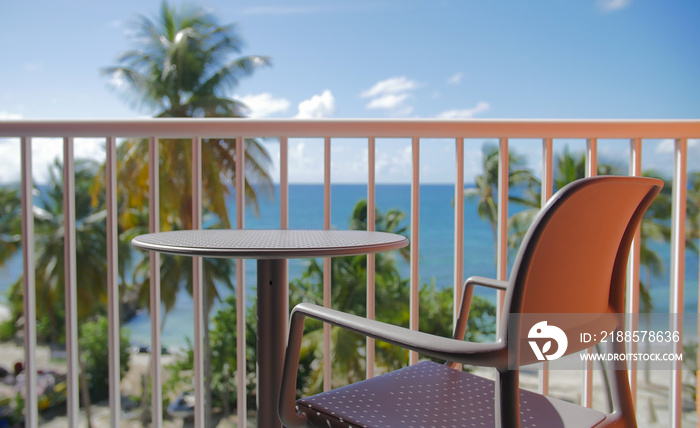 A chair and a table on a balcony with a sunny beach in background