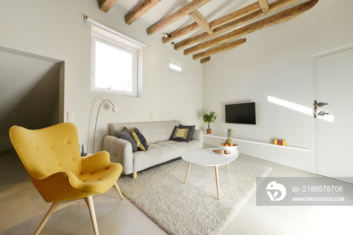 Living room with gray three-seater sofa and yellow wing-back sofa and sloping ceilings with wooden