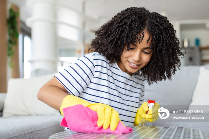 Young beautiful woman tidying up the living room and wiping the dining table surface with a cloth.