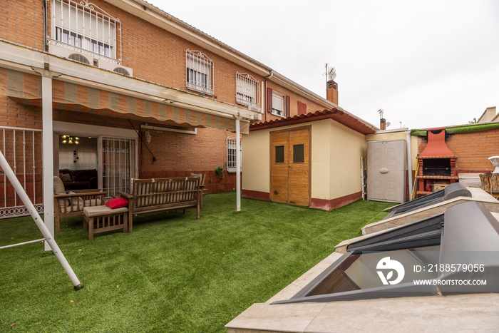 Rear terrace of a single-family home with a porch with awnings, artificial grass floors and a storag