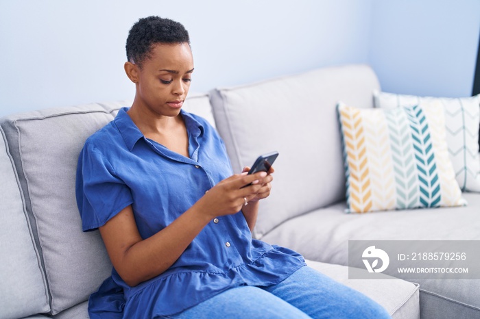 African american woman using smartphone sitting on sofa at home