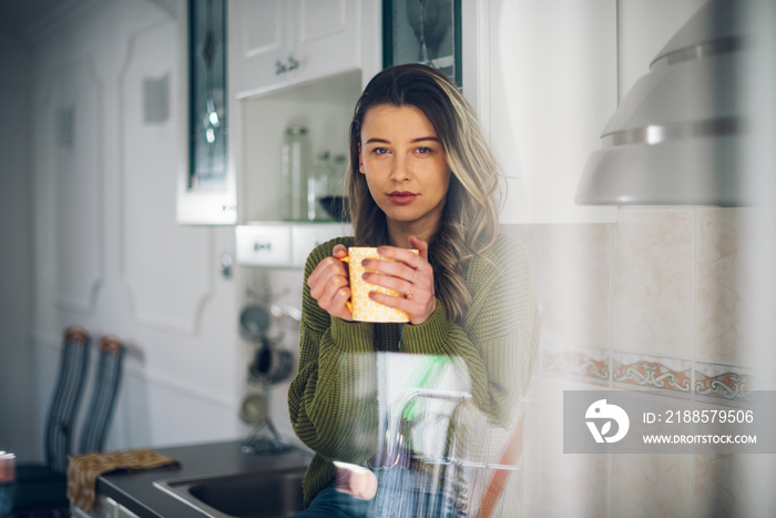 Woman standing in the kitchen and drinking cup of tea