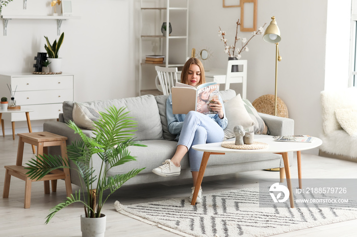 Young woman reading magazine on grey couch at home